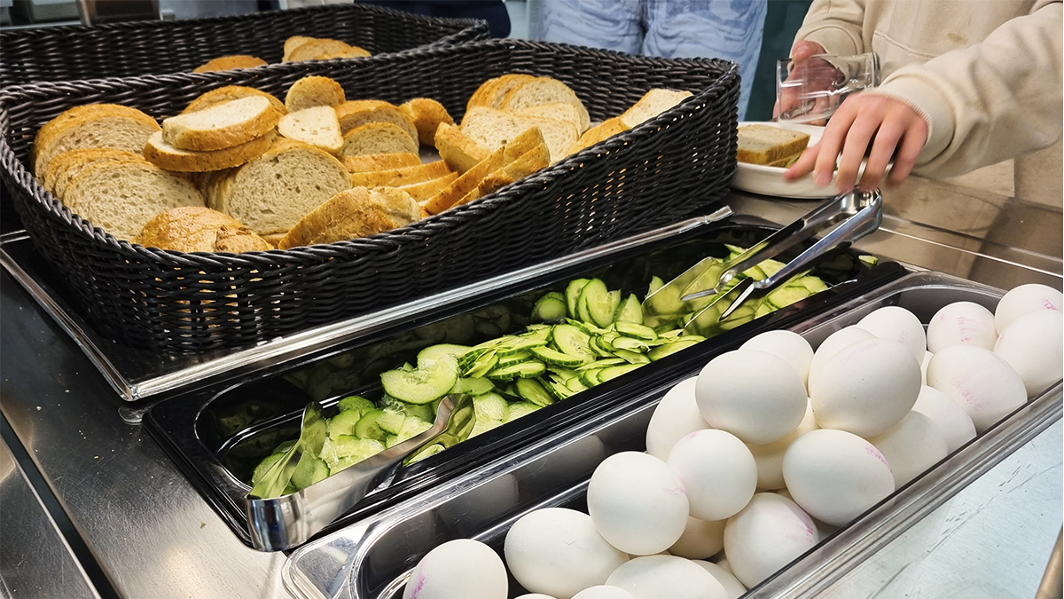 Kuvassa lapsi on linjastolla, jossa on tarjolla leipää, kurkunviipaleita ja kananmunia.