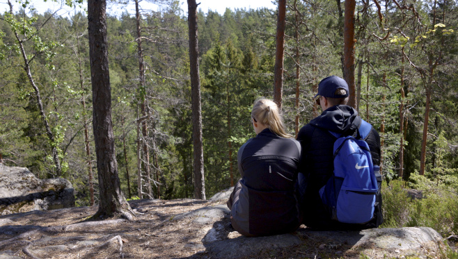En flicka och en pojke sitter på en klippa i skogen.
