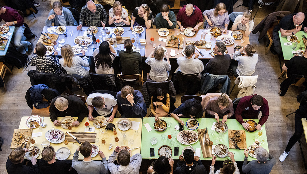 Naisia ja miehiä yhdessä rennosti ruokailemassa pitkien pöytien ääressä.