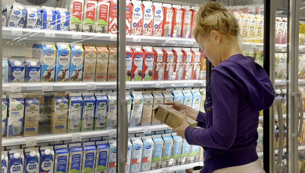 Nainen valitsee tuotetta maitohyllystä ja lukee kädessään pitämänsä tölkin tuoteselostetta.